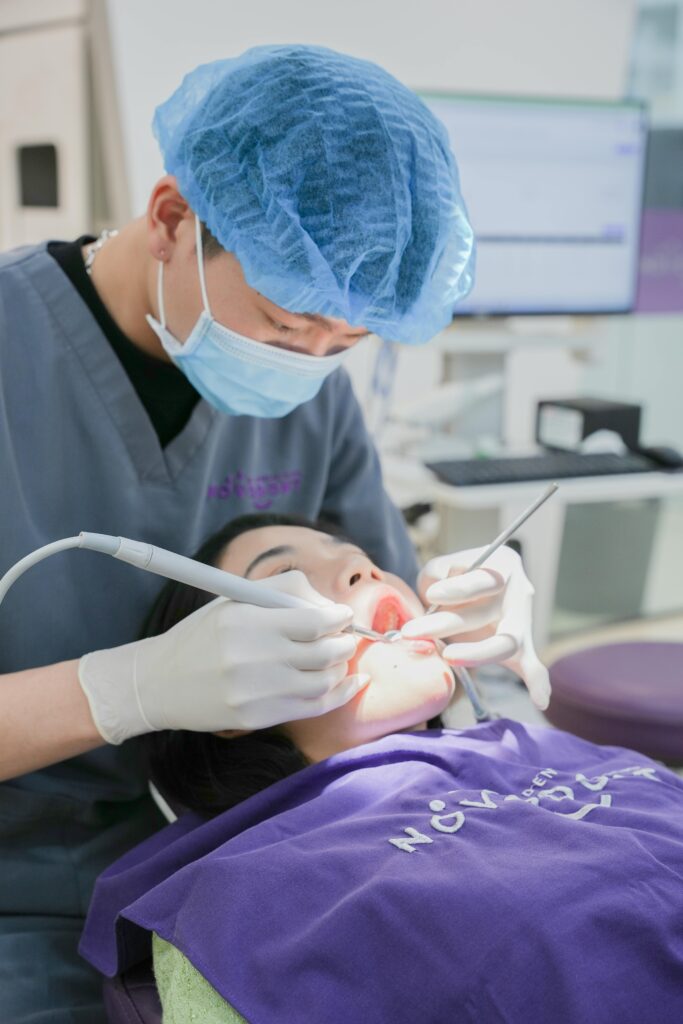 A dentist wearing a surgical mask and cap is treating a patient in a dental clinic.